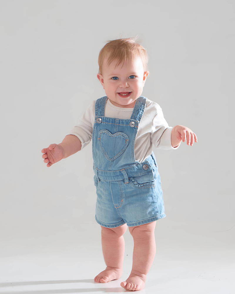 Child wearing a fluffy white snowsuit with bear ears sitting on grass.
