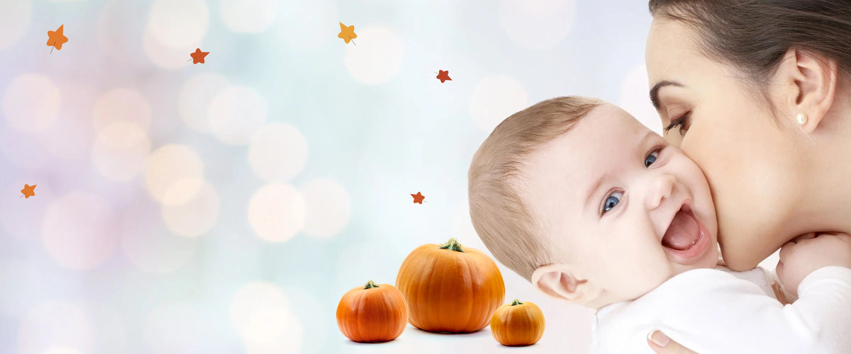 Mother kissing her smiling baby, with pumpkins for Halloween