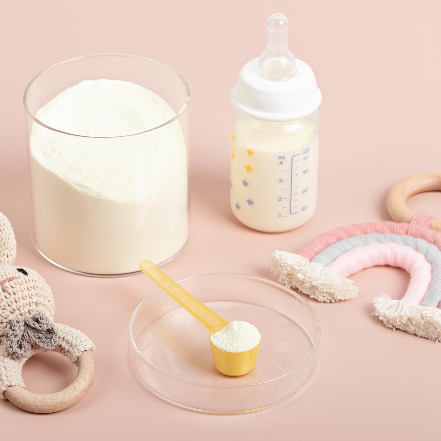 Baby formula powder, scoop and bottle on a soft pink background